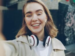 Junge Frau lächelt und fotografiert sich mit dem Smartphone beim Selfie im Freien, Fokus auf natürliche Umgebung.