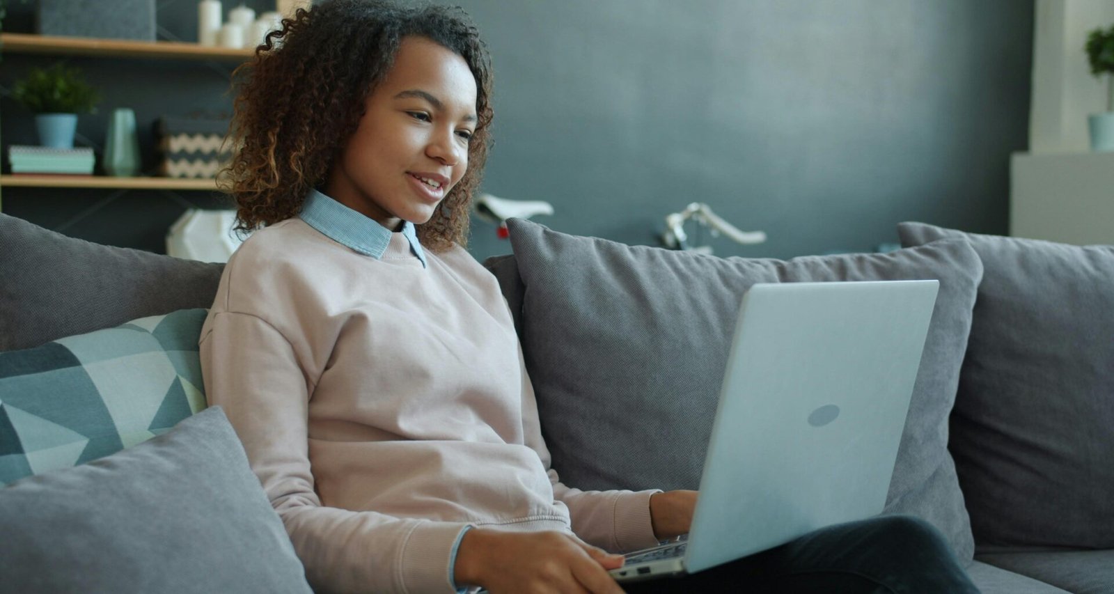 Junge Frau sitzt auf einem Sofa und arbeitet an einem Laptop, Alltagsszene mit moderner Technologie
