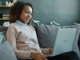 Junge Frau sitzt auf einem Sofa und arbeitet an einem Laptop, Alltagsszene mit moderner Technologie
