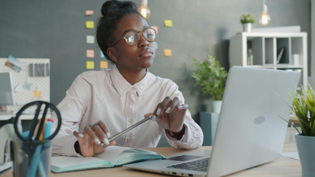Junge Frau mit Brille sitzt an einem Schreibtisch und arbeitet am Laptop in einem modernen Büro