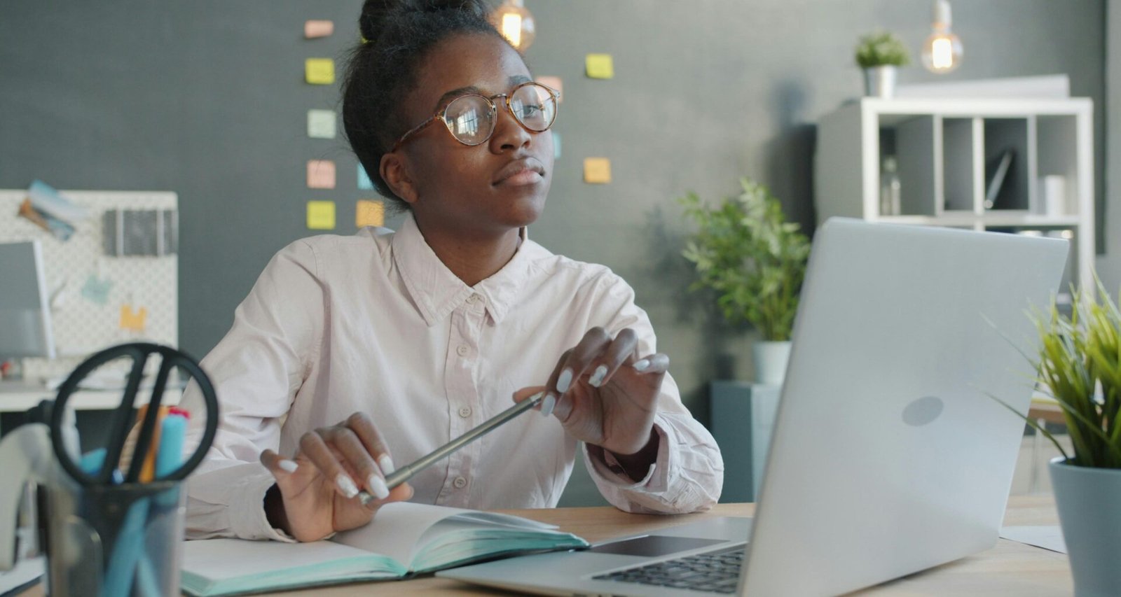 Junge Frau mit Brille sitzt an einem Schreibtisch und arbeitet am Laptop in einem modernen Büro