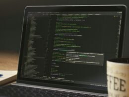 Ein Laptopbildschirm mit geöffnetem Code-Editor und einer weißen Kaffeetasse daneben auf einem Tisch.