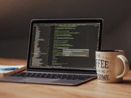 Offener Laptop mit angezeigtem Programmiercode, daneben eine weiße Kaffeetasse auf einem Tisch
