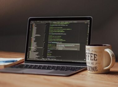 Offener Laptop mit angezeigtem Programmiercode, daneben eine weiße Kaffeetasse auf einem Tisch