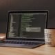 Offener Laptop mit angezeigtem Programmiercode, daneben eine weiße Kaffeetasse auf einem Tisch
