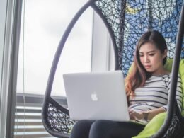 Eine Frau arbeitet mit einem MacBook auf dem Schoß, entspannter Arbeitsplatz für mobiles Arbeiten im Alltag