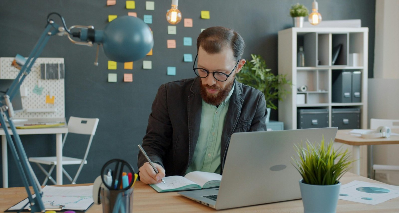Mann arbeitet an einem Schreibtisch mit Laptop und Notizbuch in einem modernen Büro