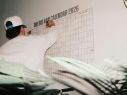 Ein Mann notiert wichtige Daten auf einem überdimensionalen Kalender für das Jahr 2026 in einem modernen Arbeitsumfeld.