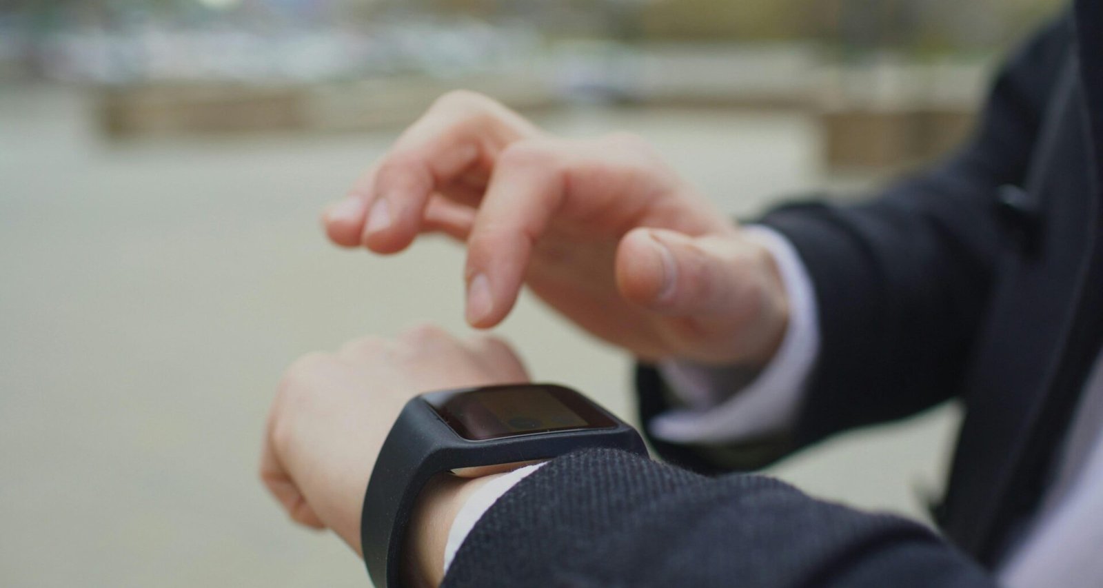 Ein Mann im Anzug steht im Freien und sieht auf seine Smartwatch, Symbolbild für mobile Technologien und digitale Organisation.