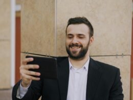 Ein Mann im Anzug sitzt und lächelt, während er auf ein Tablet blickt, in einem modernen Büro.