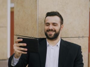 Ein Mann im Anzug sitzt und lächelt, während er auf ein Tablet blickt, in einem modernen Büro.