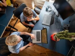 Ein Mann im grauen Langarmshirt arbeitet fokussiert an einem MacBook Pro an einem Schreibtisch mit natürlichem Licht.