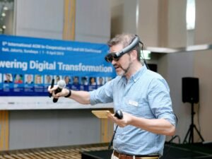 Mann im blau-weißen Karohemd hält ein kabelgebundenes Mikrofon während einer Präsentation oder Veranstaltung.