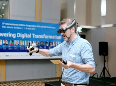 Mann im blau-weißen Karohemd hält ein kabelgebundenes Mikrofon während einer Präsentation oder Veranstaltung.