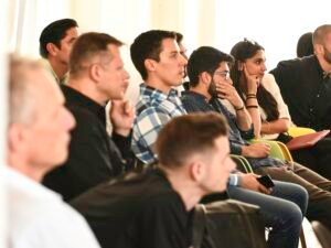 Mann mit blau-weiß kariertem Hemd auf schwarzem Stuhl, neutraler Hintergrund, passend für Business-Artikel