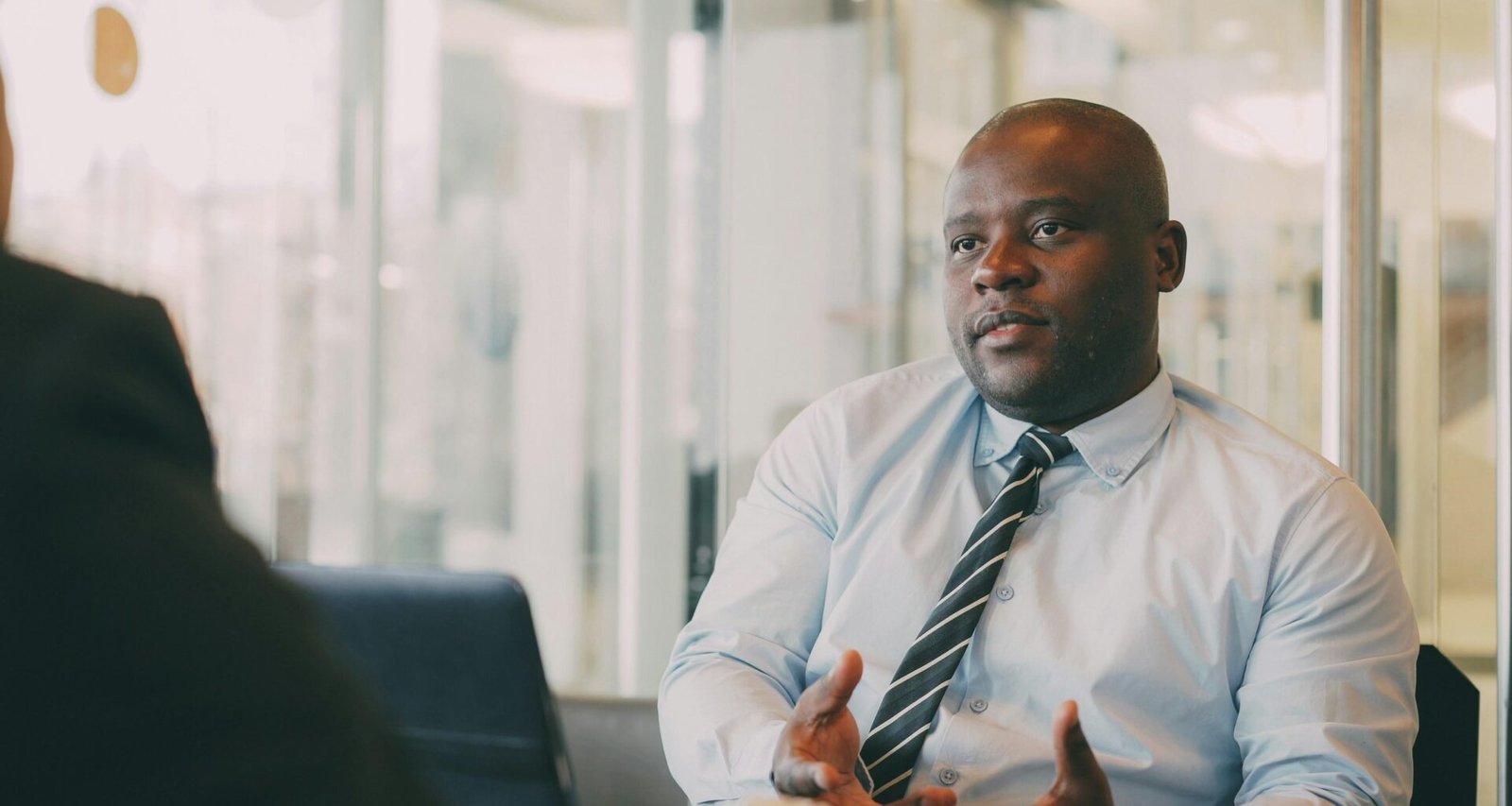 Ein Mann im hellblauen Hemd und Krawatte führt ein Gespräch in einem modernen Büroraum, Fokus auf Kommunikation.