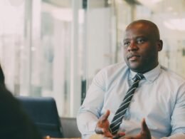 Ein Mann im hellblauen Hemd und Krawatte führt ein Gespräch in einem modernen Büroraum, Fokus auf Kommunikation.