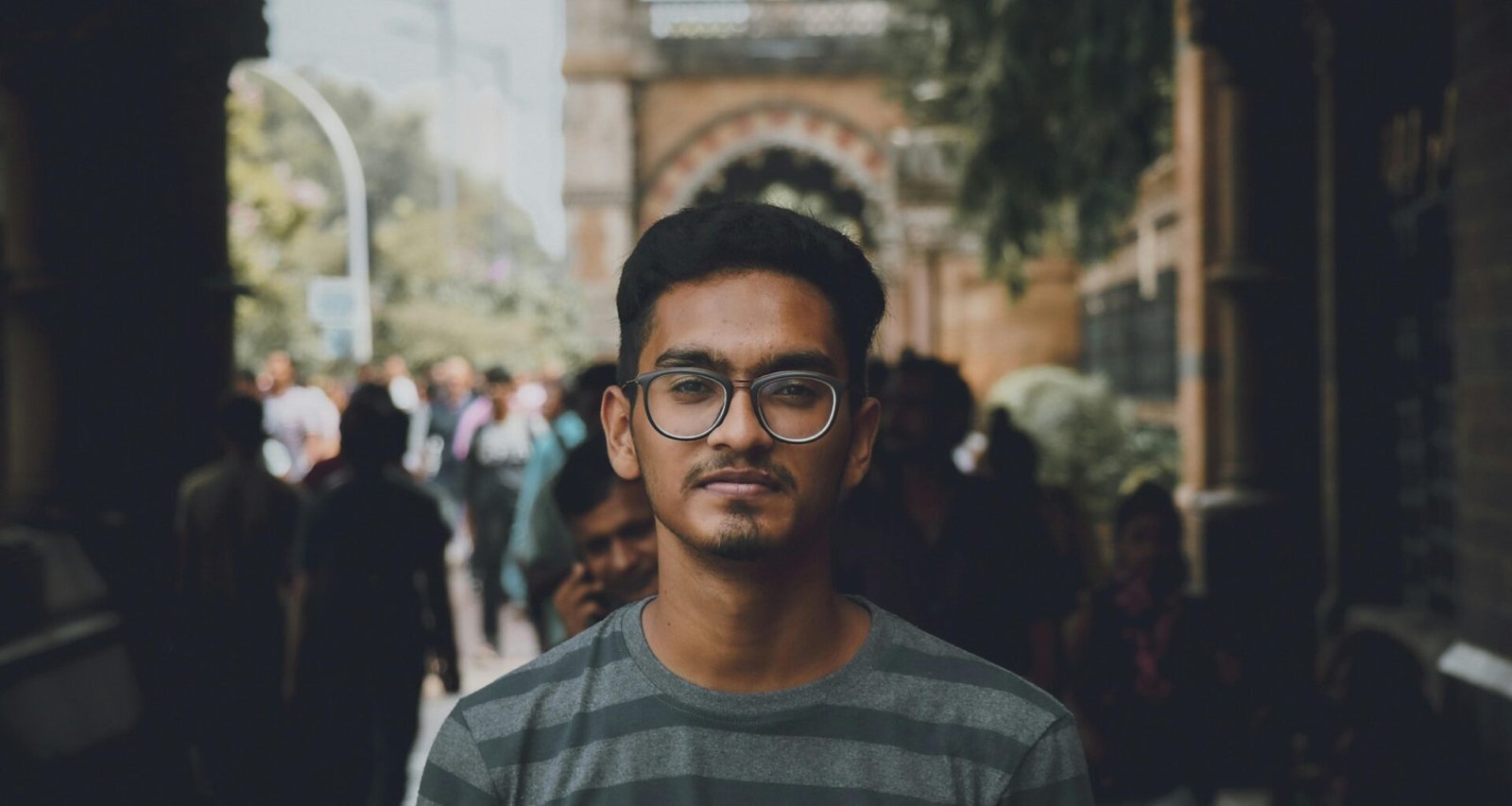 Mann mit schwarz-weiß gestreiftem Pullover und schwarzer Brille vor neutralem Hintergrund