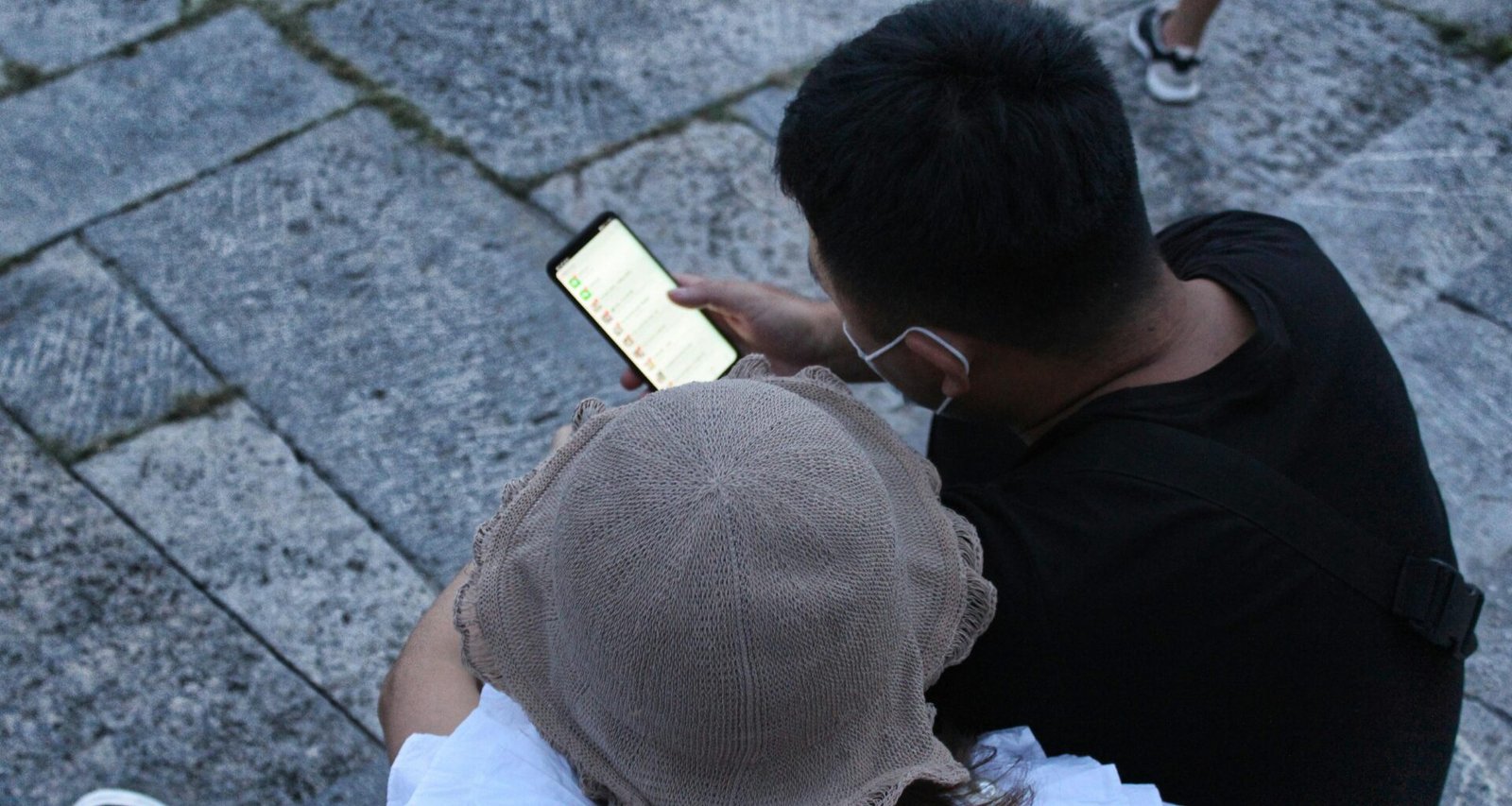 Mann in schwarzem T-Shirt und weißer Cap sitzt auf dem Boden vor neutralem Hintergrund