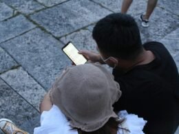 Mann in schwarzem T-Shirt und weißer Cap sitzt auf dem Boden vor neutralem Hintergrund