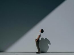 Mann mit weißem T-Shirt und weißen Shorts steht vor einer weißen Wand in minimalistischem Umfeld
