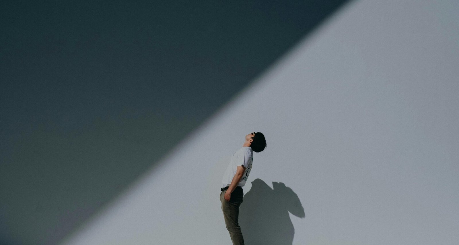 Ein Mann trägt ein weißes T-Shirt und weiße Shorts und steht entspannt an einer weißen Wand, minimalistisch und modern inszeniert.