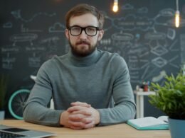 Mann mit Brille sitzt an einem Schreibtisch im hellen Büro und arbeitet am Computer, moderne Büroatmosphäre