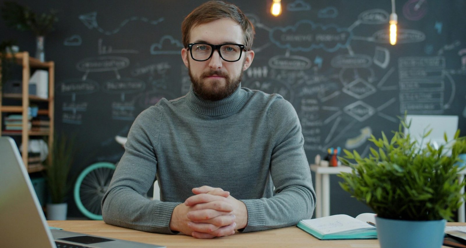 Mann mit Brille sitzt an einem Schreibtisch in einem modernen Büro und arbeitet am Computer