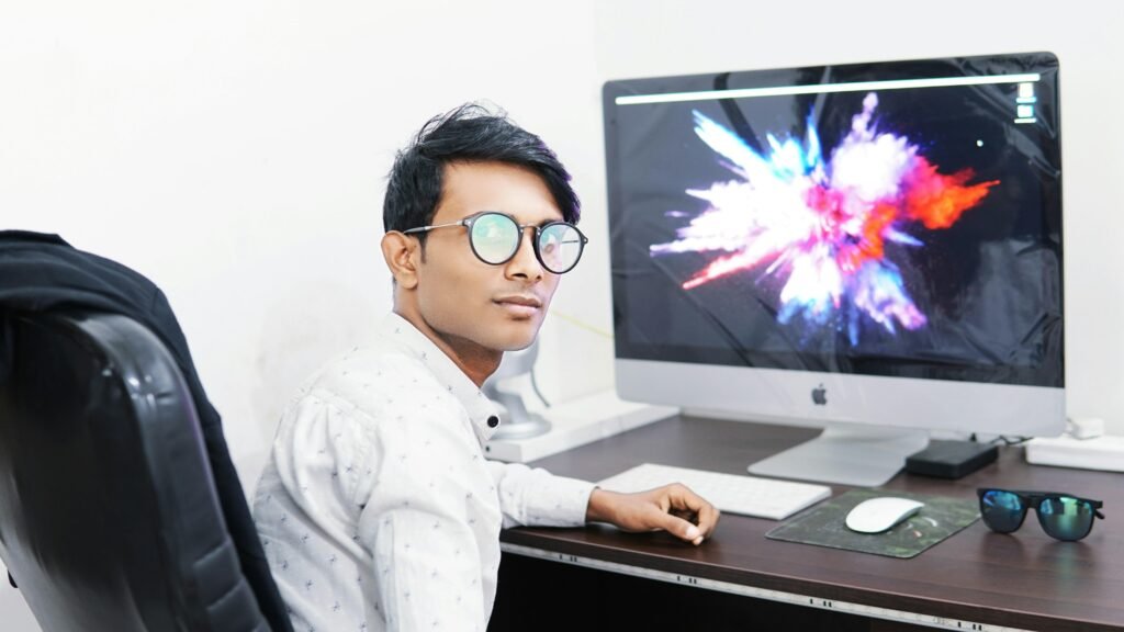 Mann arbeitet konzentriert an einem iMac in einem modernen Büro mit Tageslicht und stilvollem Arbeitsplatz.