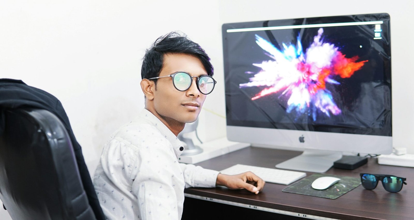 Mann arbeitet konzentriert an einem iMac in einem modernen Büro mit Tageslicht und stilvollem Arbeitsplatz.