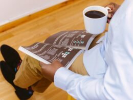 Mann sitzt mit weißer Kaffeetasse und liest konzentriert ein Magazin am Tisch in heller Umgebung