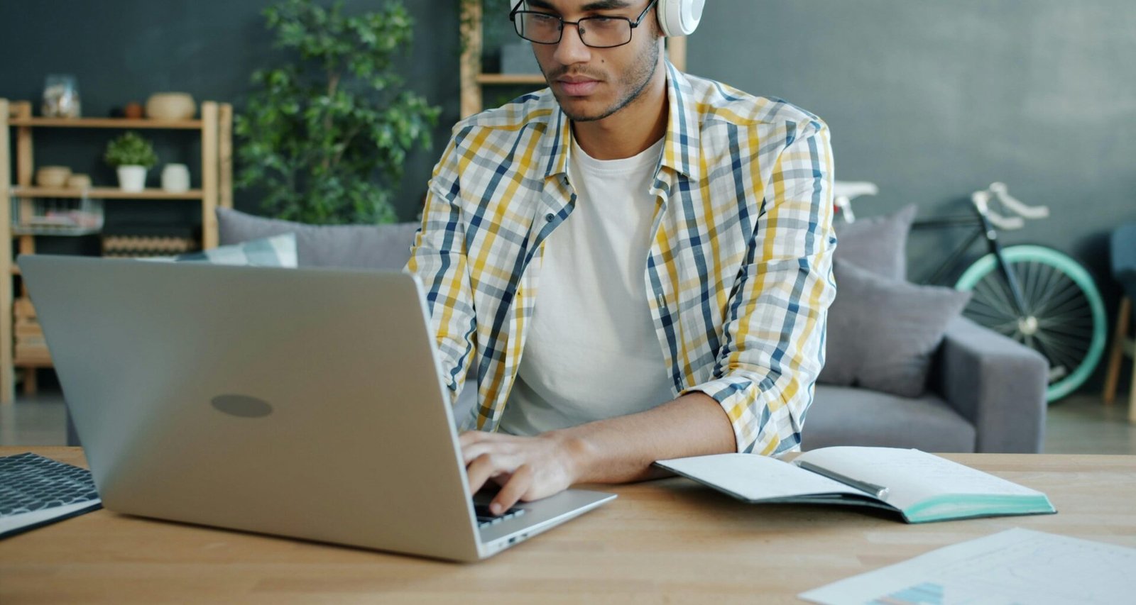 Mann mit Kopfhörern arbeitet an einem Laptop am Schreibtisch in einem modernen Büro, konzentriert auf seine Aufgaben