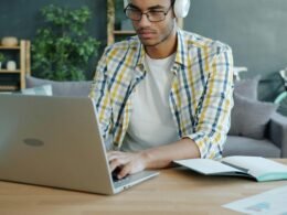 Mann mit Kopfhörern arbeitet an einem Laptop am Schreibtisch in einem modernen Büro, konzentriert auf seine Aufgaben
