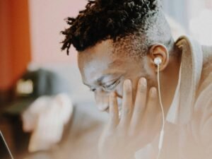 Mann mit Kopfhörern sitzt lachend vor einem Computerbildschirm in einem modernen Büro