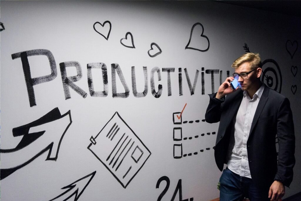 Ein Mann hält ein Smartphone in der Hand und betrachtet eine Wanddekoration mit Produktivitätsmotiven in einem modernen Raum.
