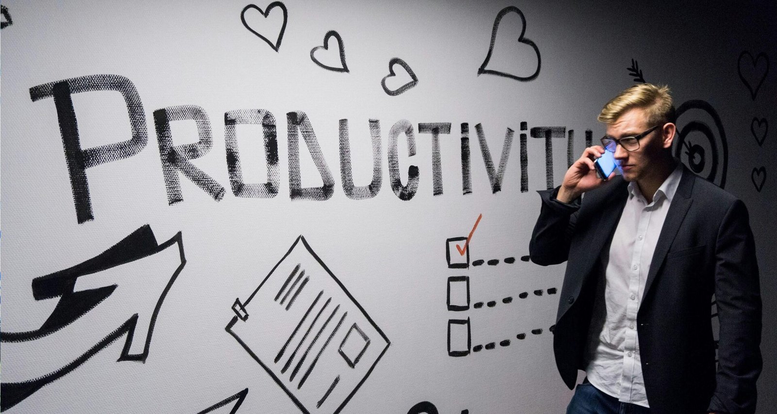 Ein Mann hält ein Smartphone in der Hand und betrachtet eine Wanddekoration mit Produktivitätsmotiven in einem modernen Raum.
