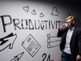 Ein Mann hält ein Smartphone in der Hand und betrachtet eine Wanddekoration mit Produktivitätsmotiven in einem modernen Raum.