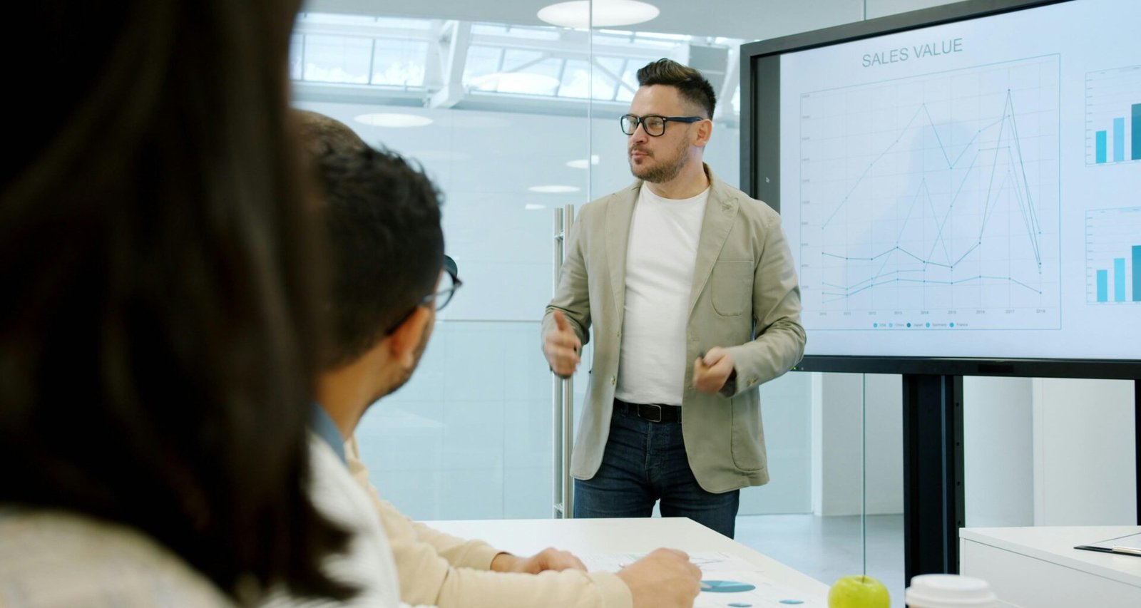 Mann erklärt Kolleginnen und Kollegen im Büro Daten auf einem großen Bildschirm während einer Besprechung.