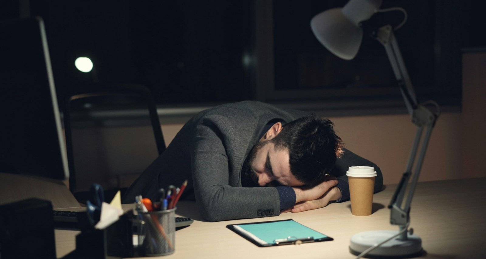 Mann schläft am Schreibtisch neben einer Kaffeetasse und einem Tablet, symbolisch für Müdigkeit im Arbeitsalltag.