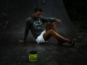 Ein Mann sitzt lässig auf den Gleisen eines Skatepark-Skateboards, industrielle Umgebung im Hintergrund