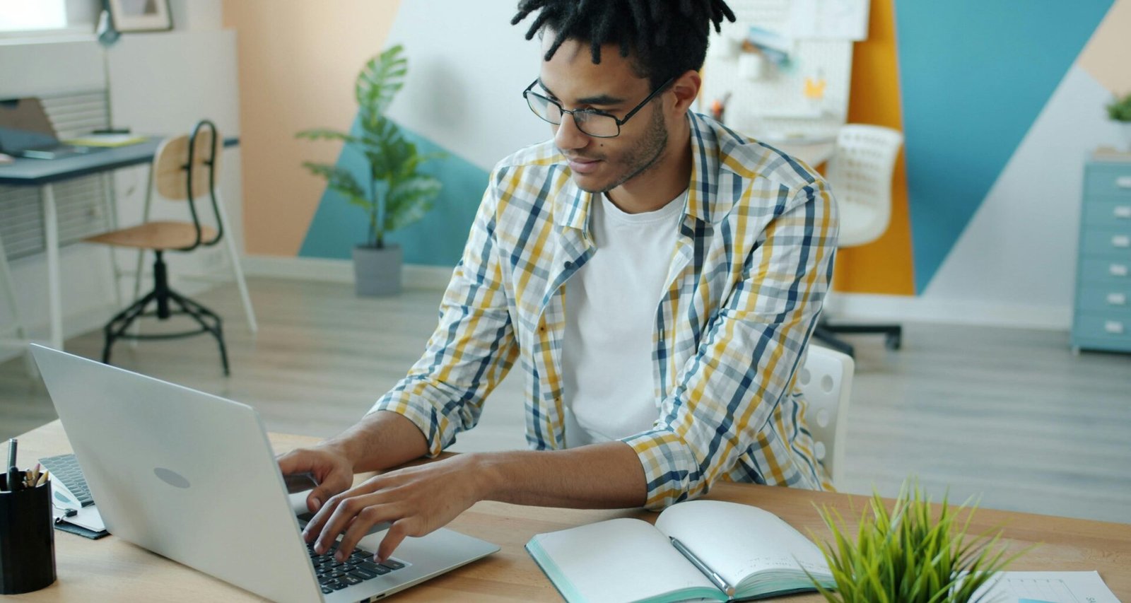 Mann arbeitet an einem Laptop am Schreibtisch mit Notizbuch für effizientes Online-Marketing und Technologieaufgaben