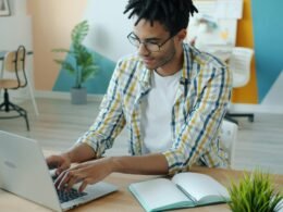 Mann arbeitet an einem Laptop am Schreibtisch mit Notizbuch für effizientes Online-Marketing und Technologieaufgaben