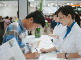 Ein Mann unterschreibt ein Dokument an einem Service-Schalter im öffentlichen Bereich, Fokus auf Kundendienst und Verwaltung