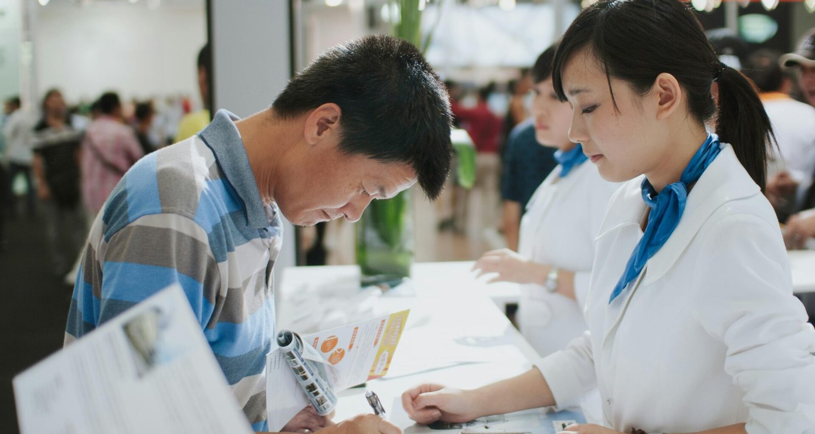 Ein Mann sitzt an einem Serviceschalter und unterschreibt ein offizielles Dokument, Aufnahme im modernen Innenbereich