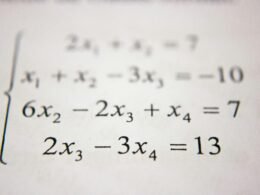 Schreibtisch mit Zettel voll mathematischer Formeln und Berechnungen, Fokus auf handschriftliche Mathematik