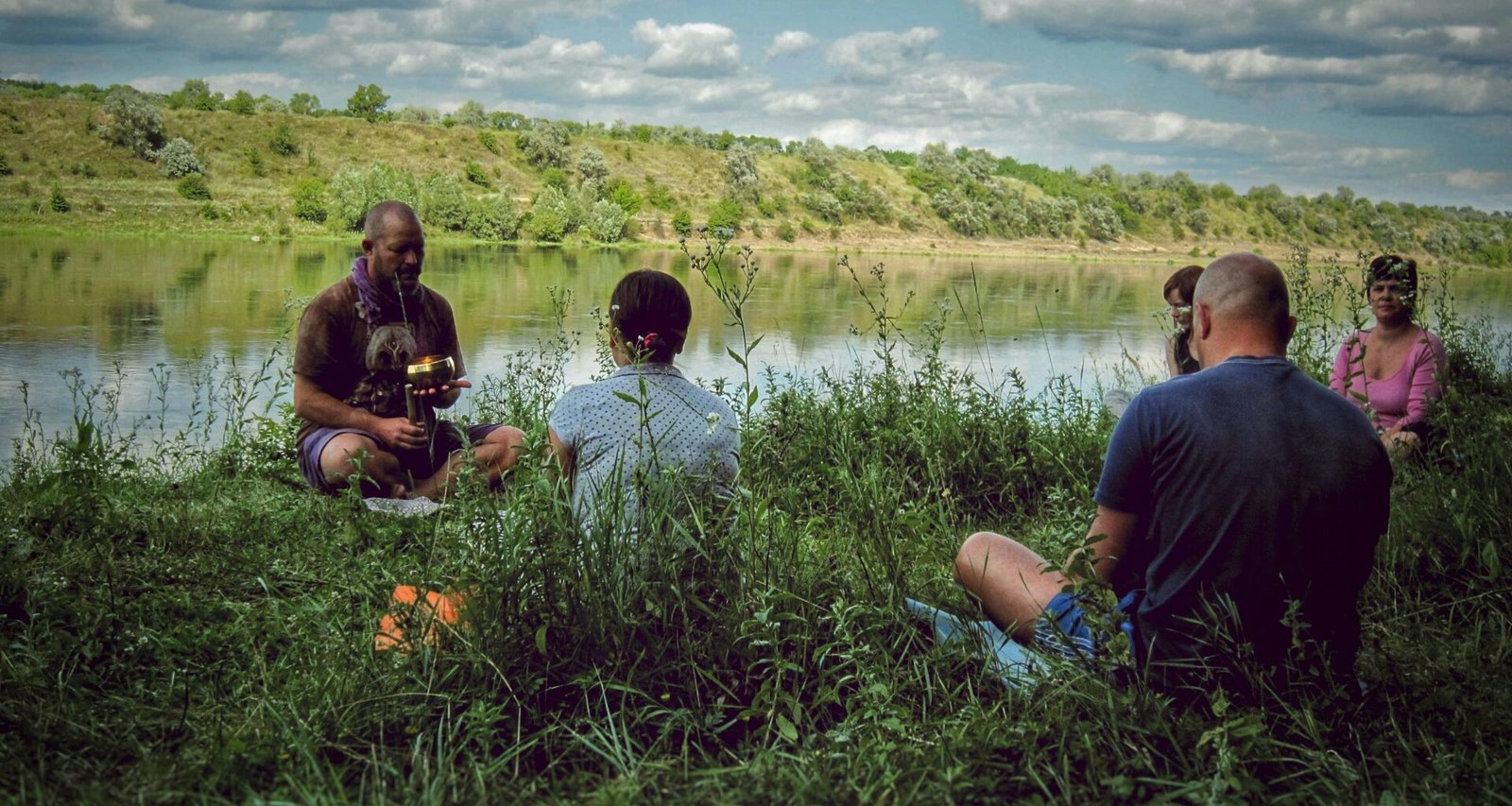Mehrere Personen befinden sich am Ufer eines Sees, umgeben von natürlicher Landschaft und Wasserfläche