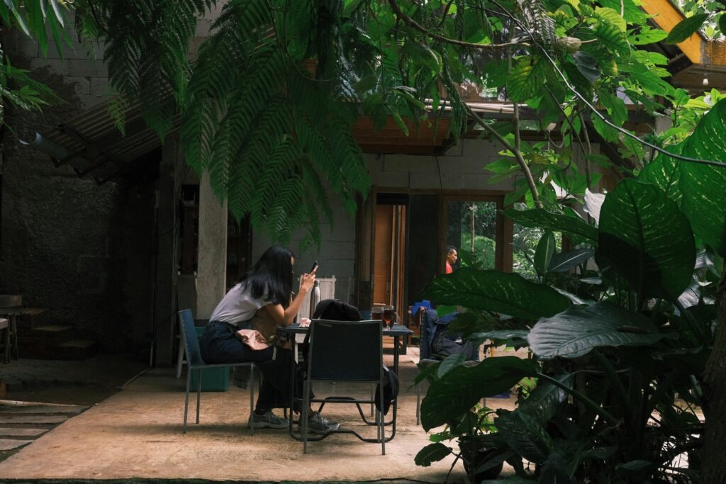 Menschen sitzen an mehreren Tischen in einem von vielen Pflanzen beschatteten Open-Air-Café und unterhalten sich.