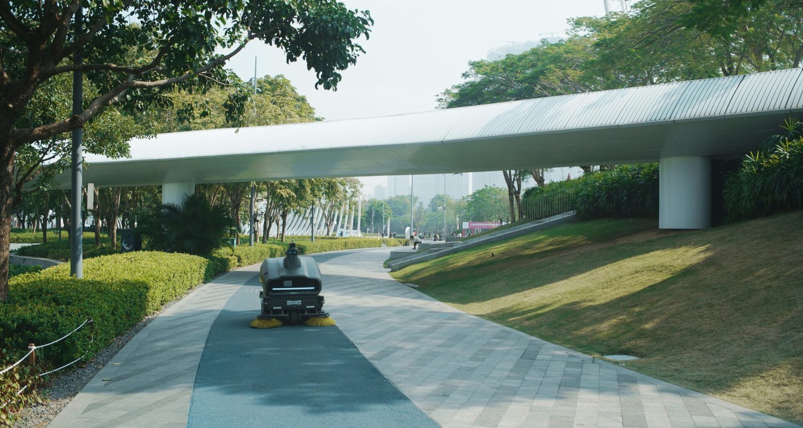 Moderne Fußgängerbrücke mit klaren Linien führt über einen grünen Parkweg und verbindet zwei Bereiche der Anlage.