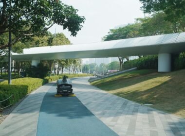 Moderne Fußgängerbrücke mit klaren Linien führt über einen grünen Parkweg und verbindet zwei Bereiche der Anlage.