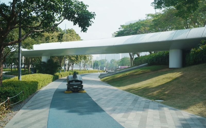 Moderne Fußgängerbrücke mit klaren Linien führt über einen grünen Parkweg und verbindet zwei Bereiche der Anlage.